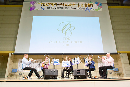 The LSO Brass Quintet performs beneath a sign made by the students of Onarimon Junior High School.
